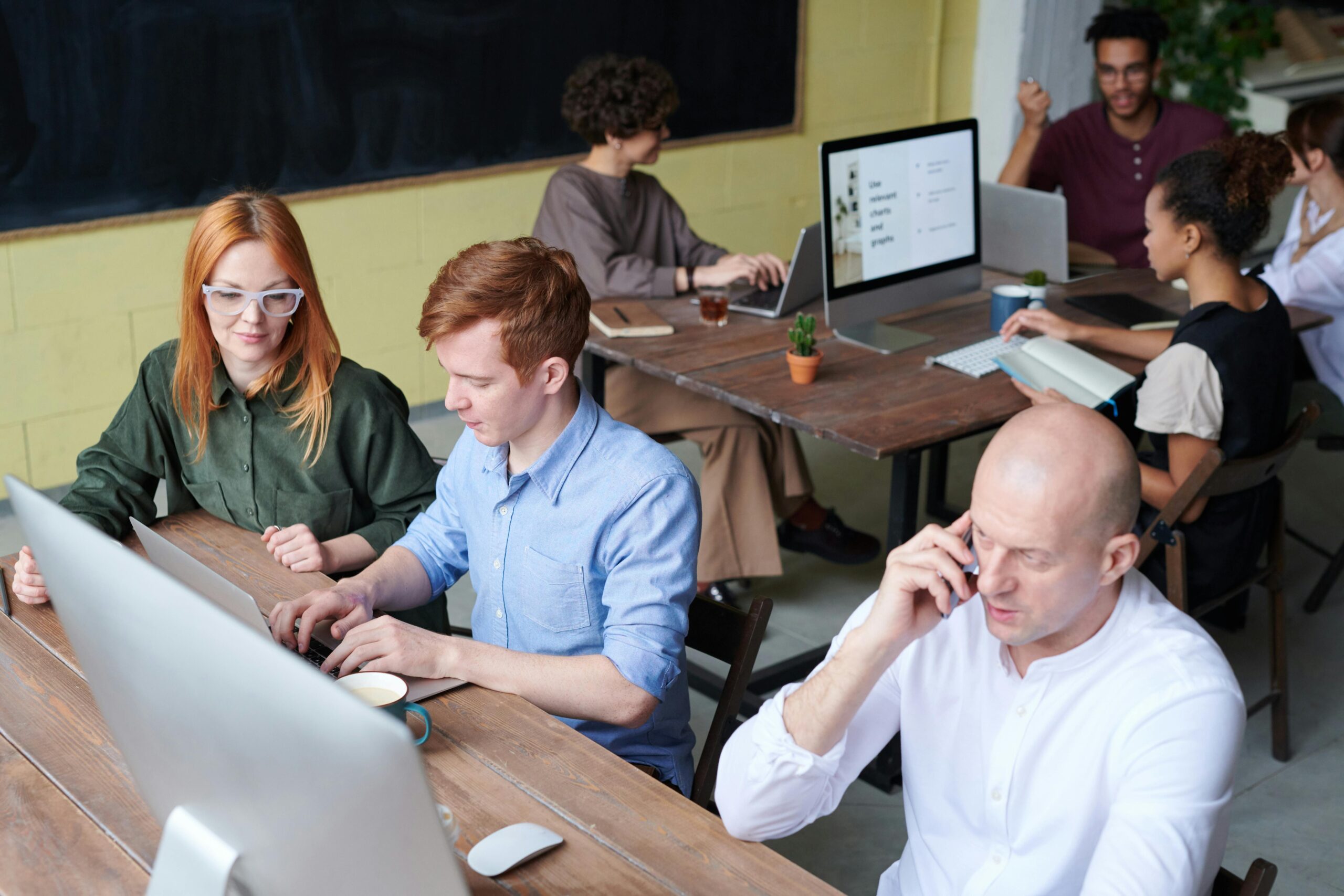 4 people working at different desks and computers